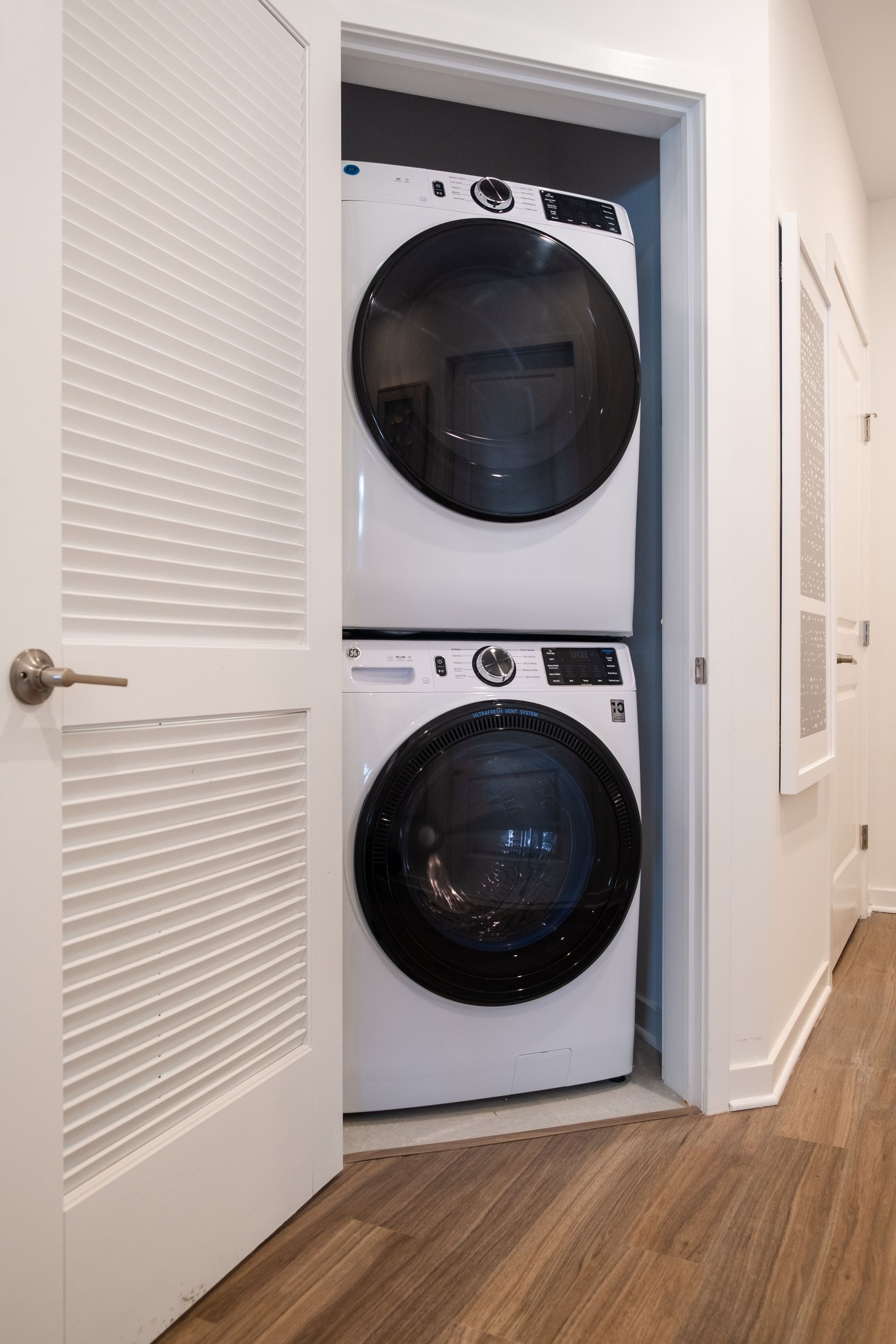 Stacked white washer and dryer in a closet, with a partially opened door.