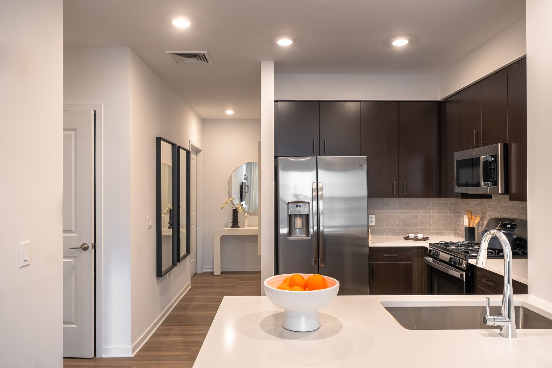 Modern kitchen with dark wood cabinets, stainless steel appliances, and white island with fruit bowl.