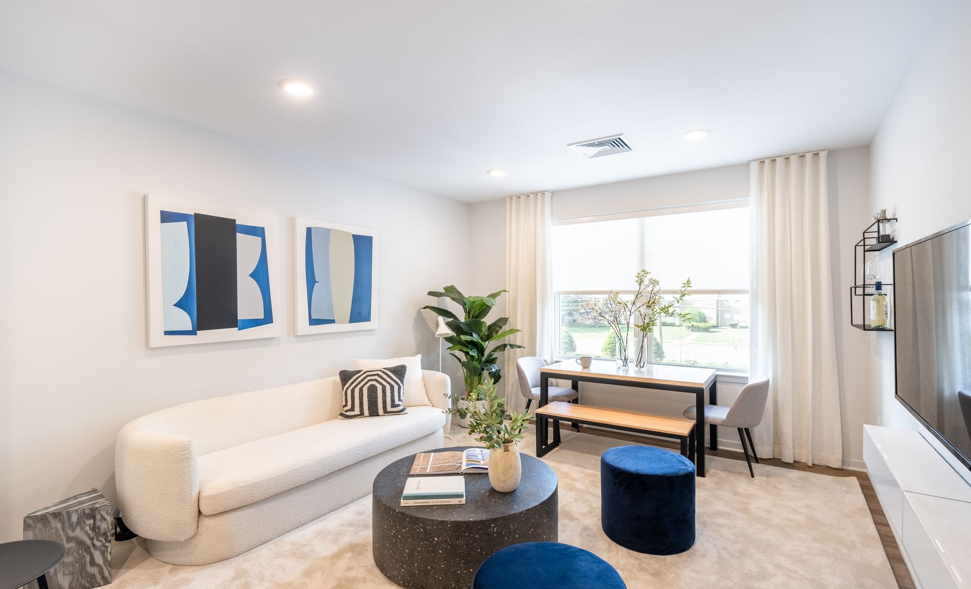 Living room with white sofa, blue artwork, and a dining table.