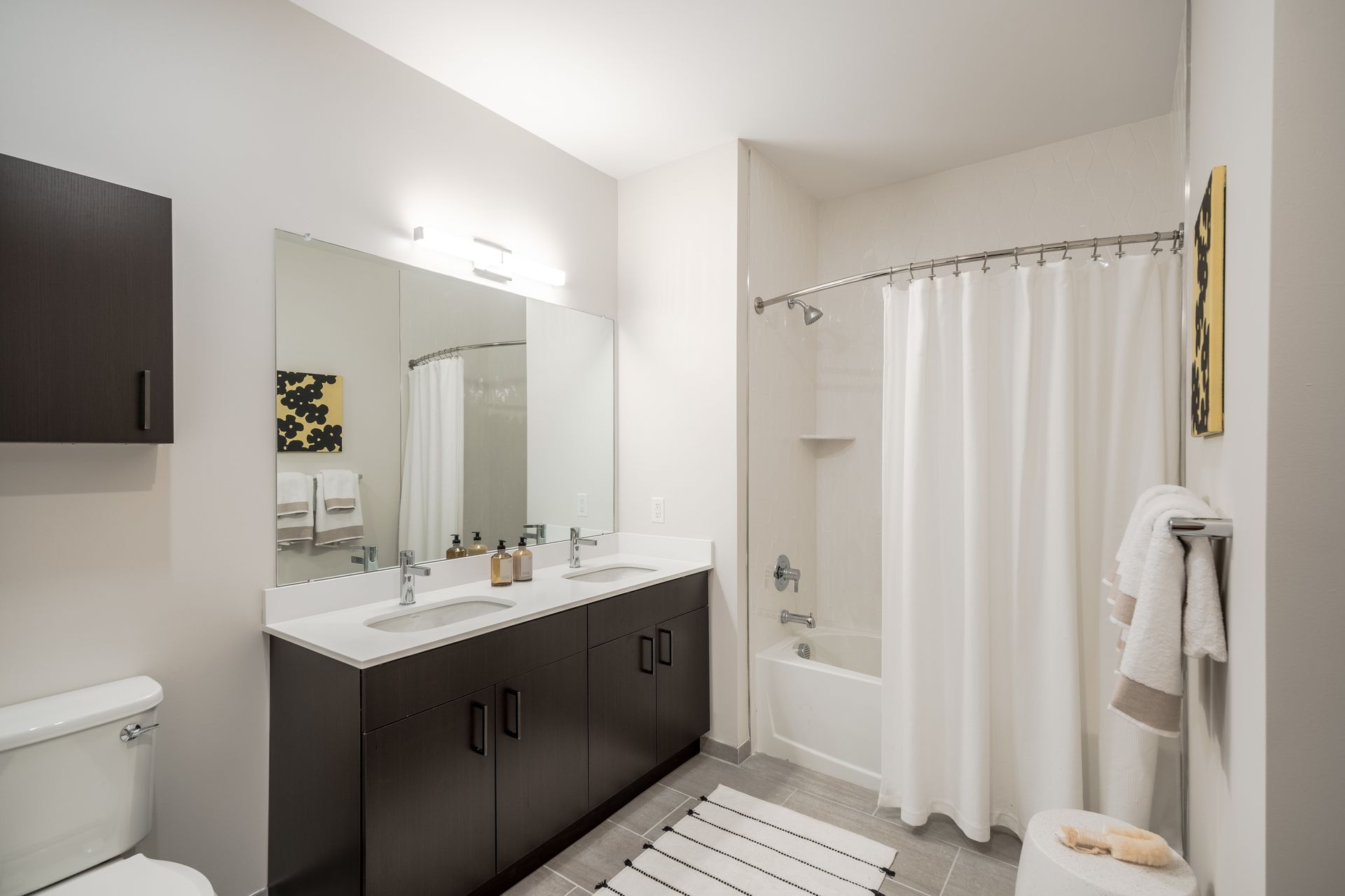 Modern bathroom with double vanity, bathtub, and toilet; neutral tones.