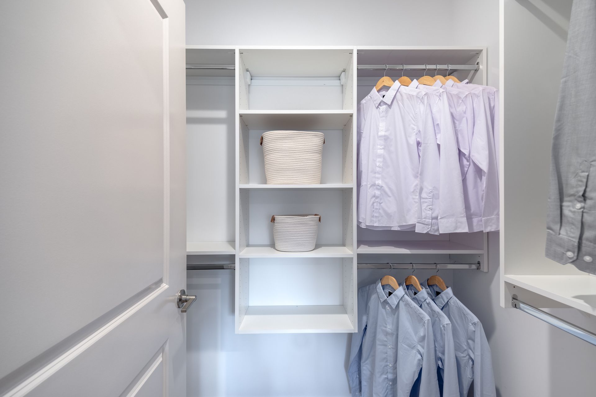 White closet with shelves, hanging shirts, and two baskets.