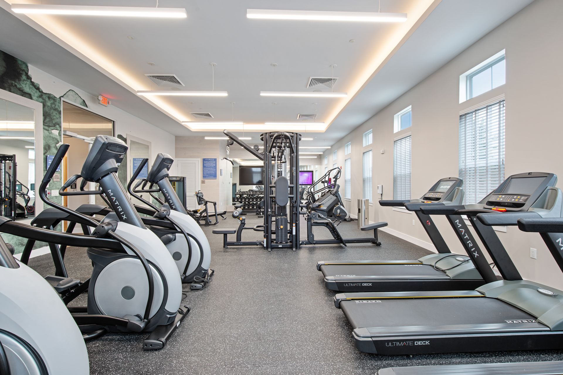 Gym with treadmills, elliptical machines, and weight machines. Bright, modern space with neutral colors.