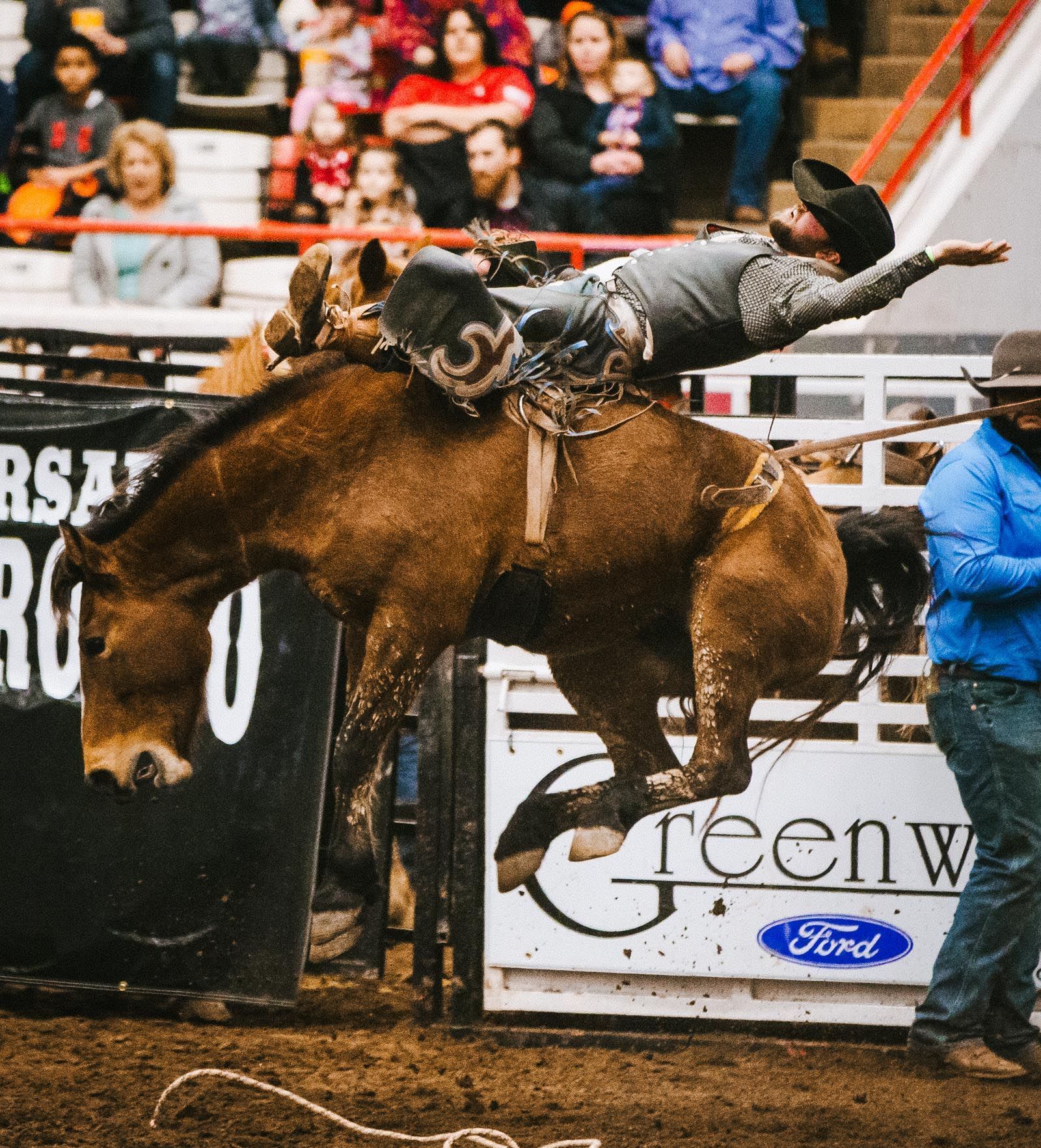 A man is riding a horse in front of a sign that says ford