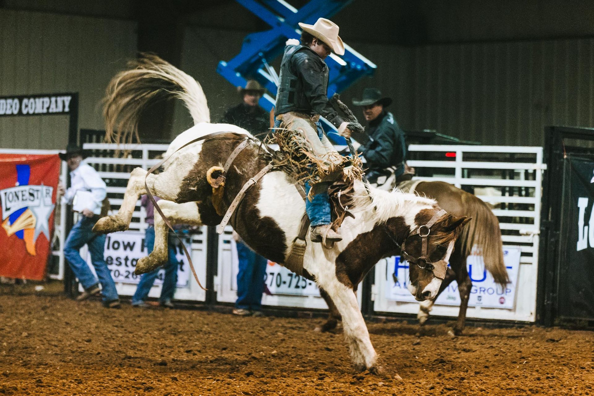 A man is riding a brown and white horse in a rodeo arena.