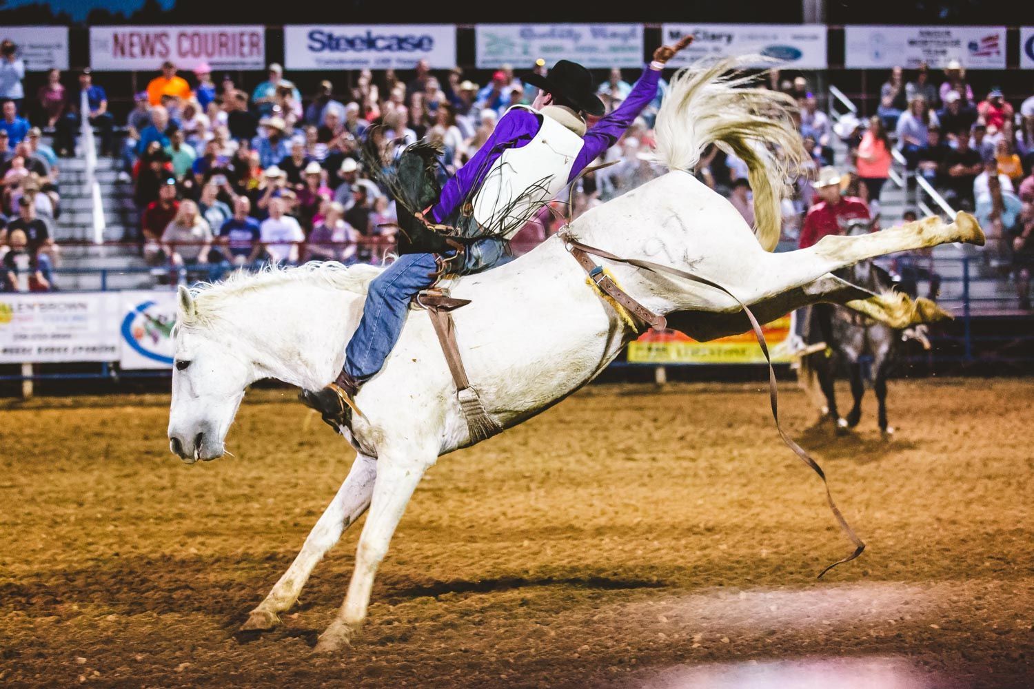 A man is riding a white horse in a rodeo arena.