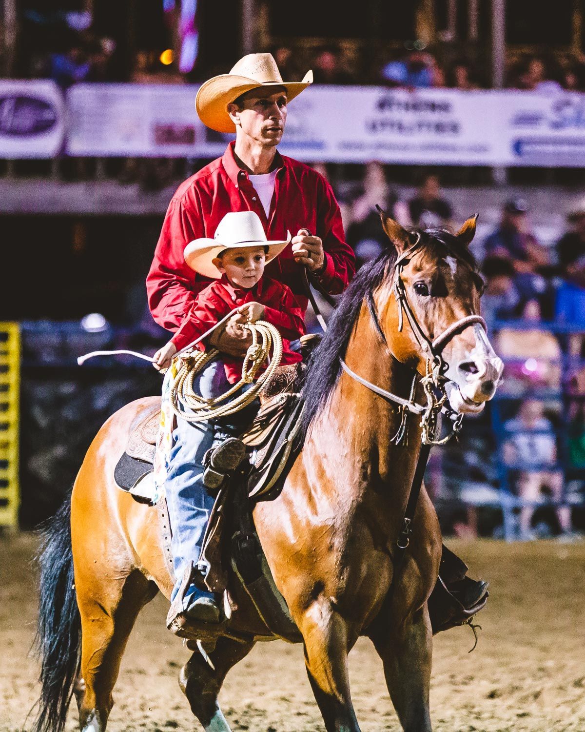 A man and a child are riding a horse at a rodeo.