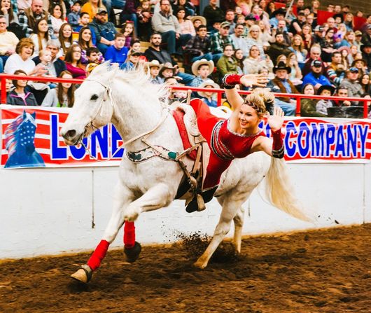 A woman is riding a white horse in front of a sign that says lone company