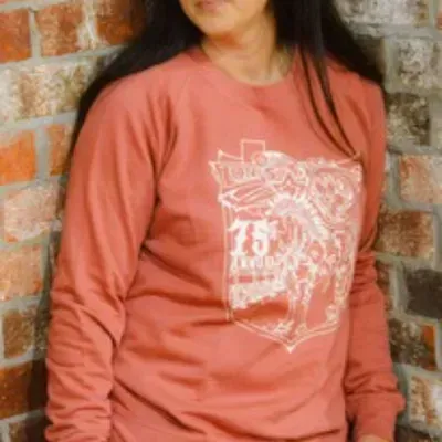 A woman wearing a long sleeve red shirt is standing in front of a brick wall.