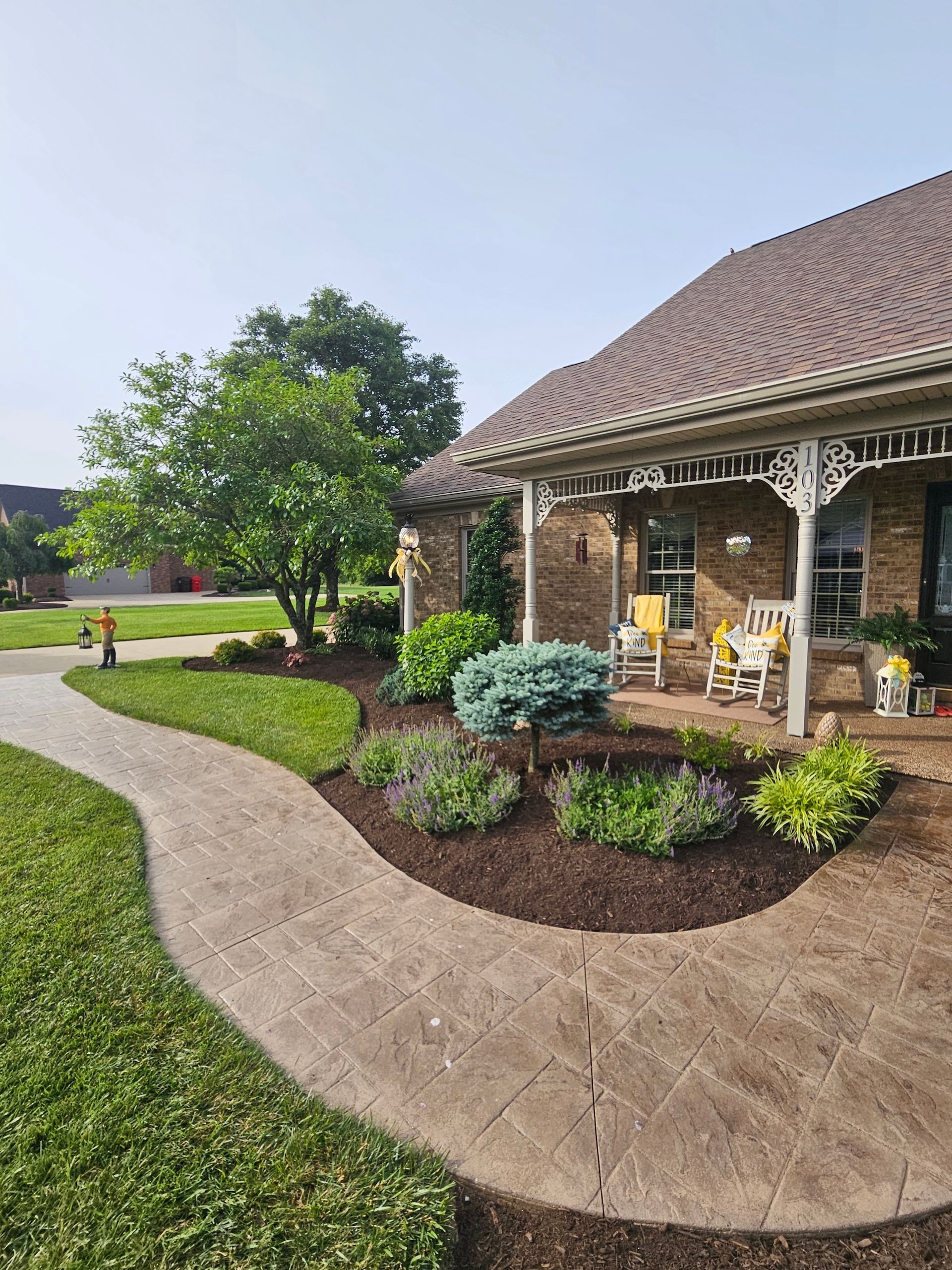 Stone walkway leads to a brick house with a porch and landscaped garden.