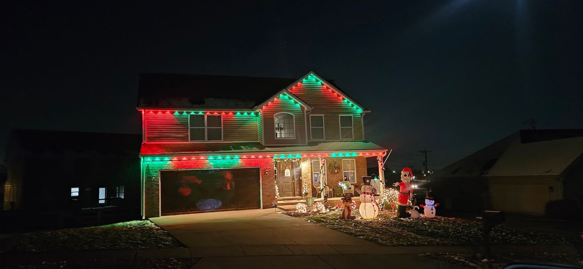 A two-story house illuminated with red and green Christmas lights at night.