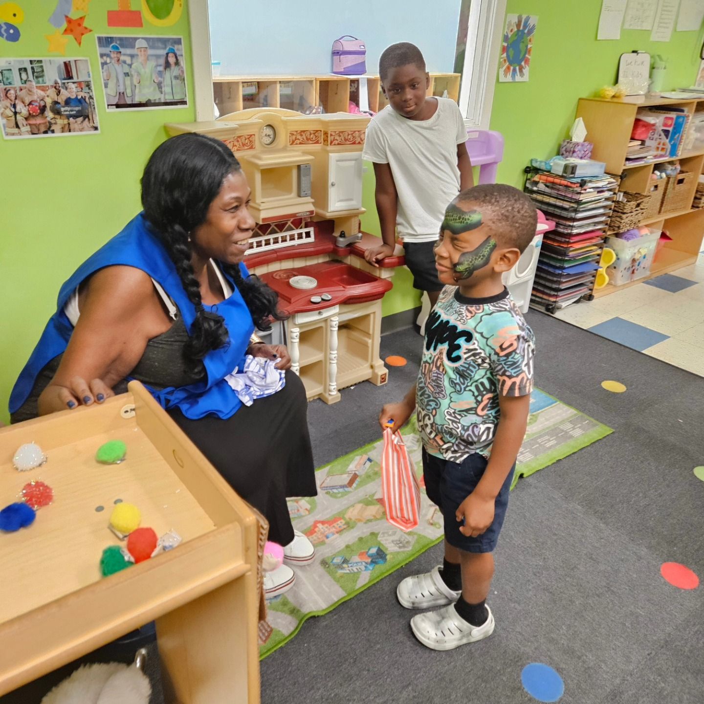 A diverse group of children sit and play on a colorful indoor playground with a treehouse mural background.