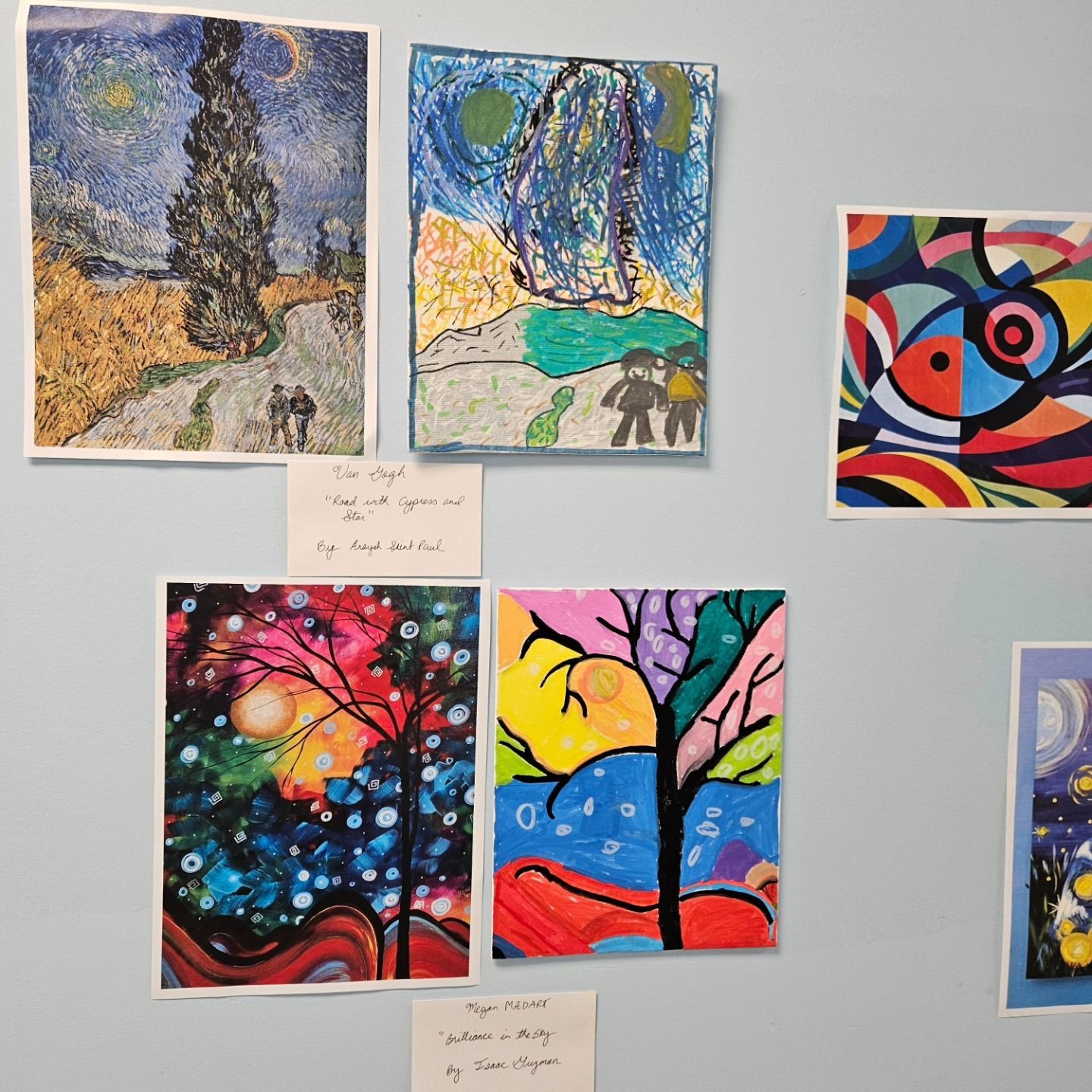 A display of colorful student artwork on a light blue wall, featuring various drawings of trees and abstract patterns.