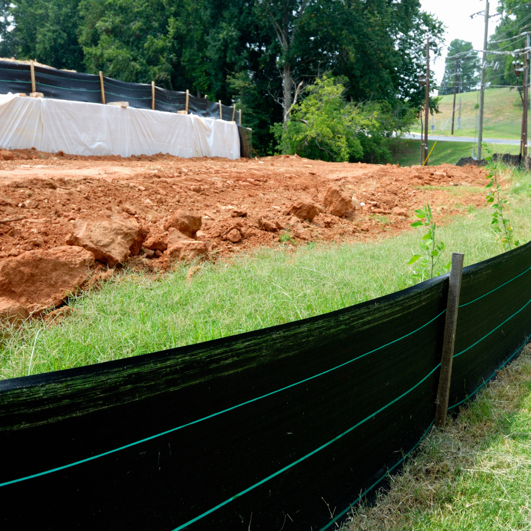 Construction site with black silt fence, bare earth, and green grass.