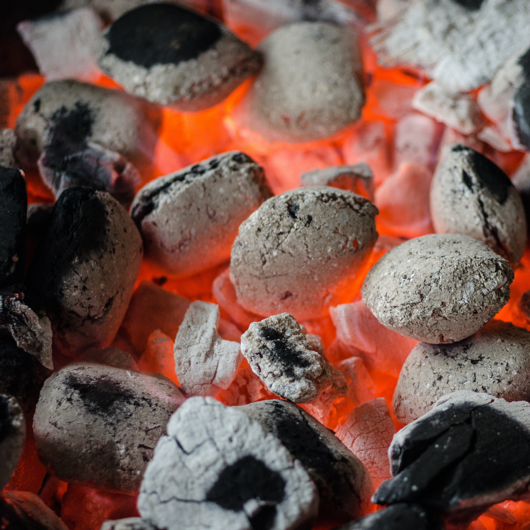 Glowing charcoal briquettes, close-up, with visible heat and ash.