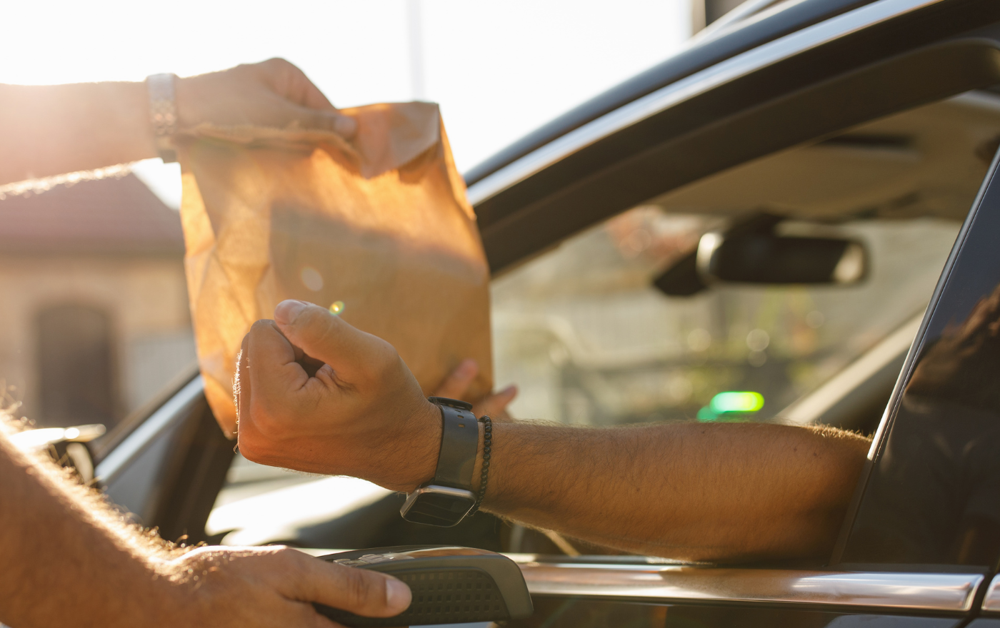 Person receiving a brown paper bag from someone at a car window, likely a drive-thru.