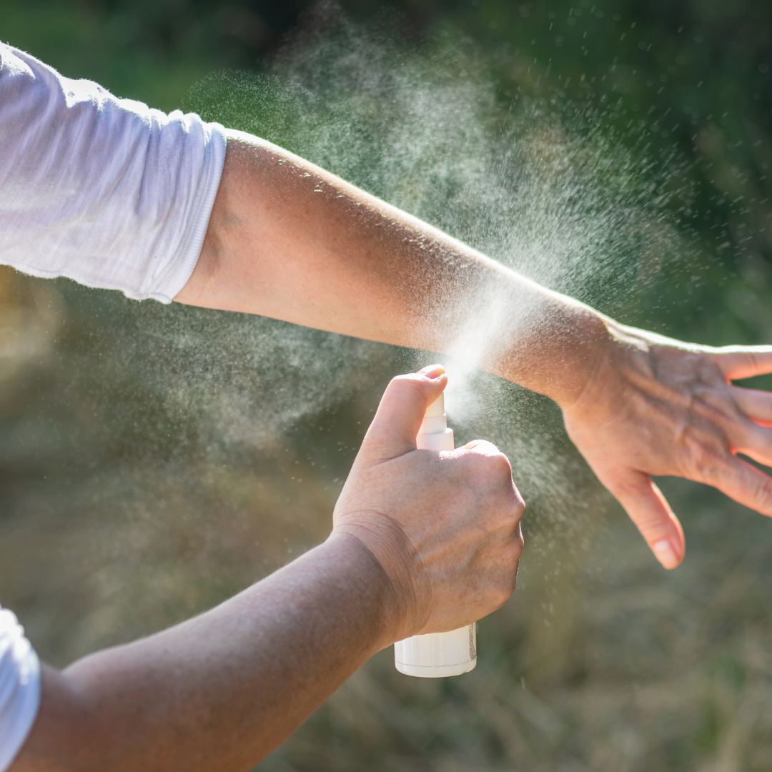 Person spraying insect repellent on arm outdoors.