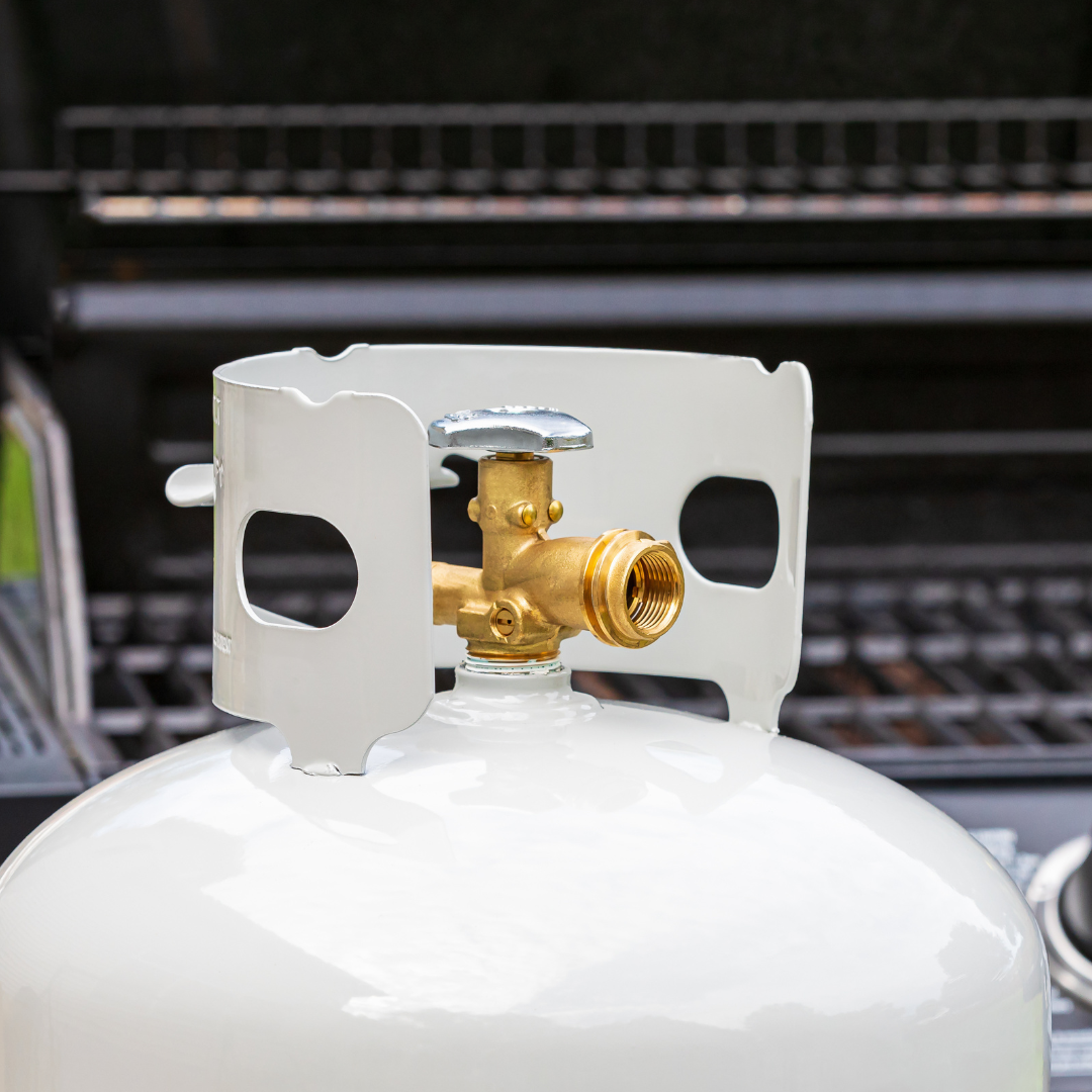 White propane tank with brass valve and grill in the background.