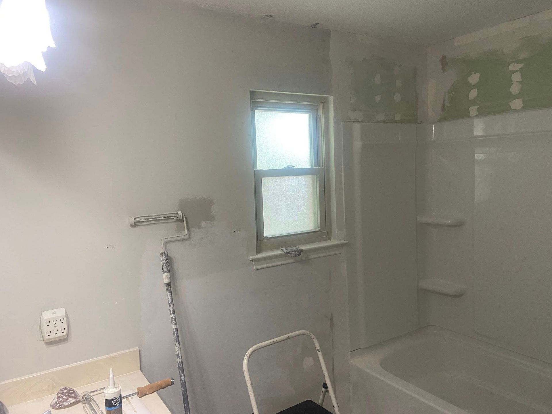 Bathroom under renovation; gray walls, white fixtures, small window, paint supplies visible.