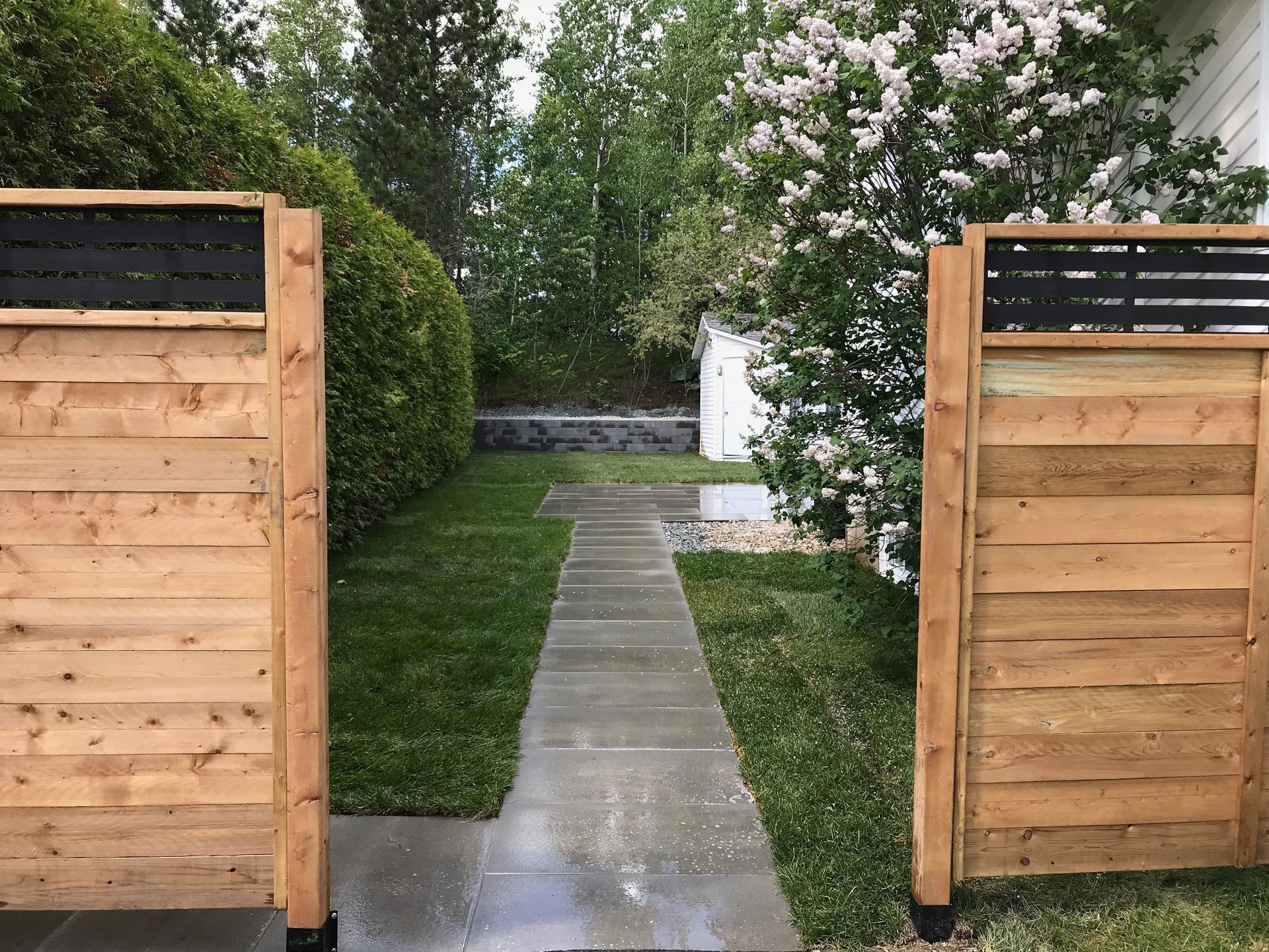 Une clôture en bois entoure une allée menant à une maison.