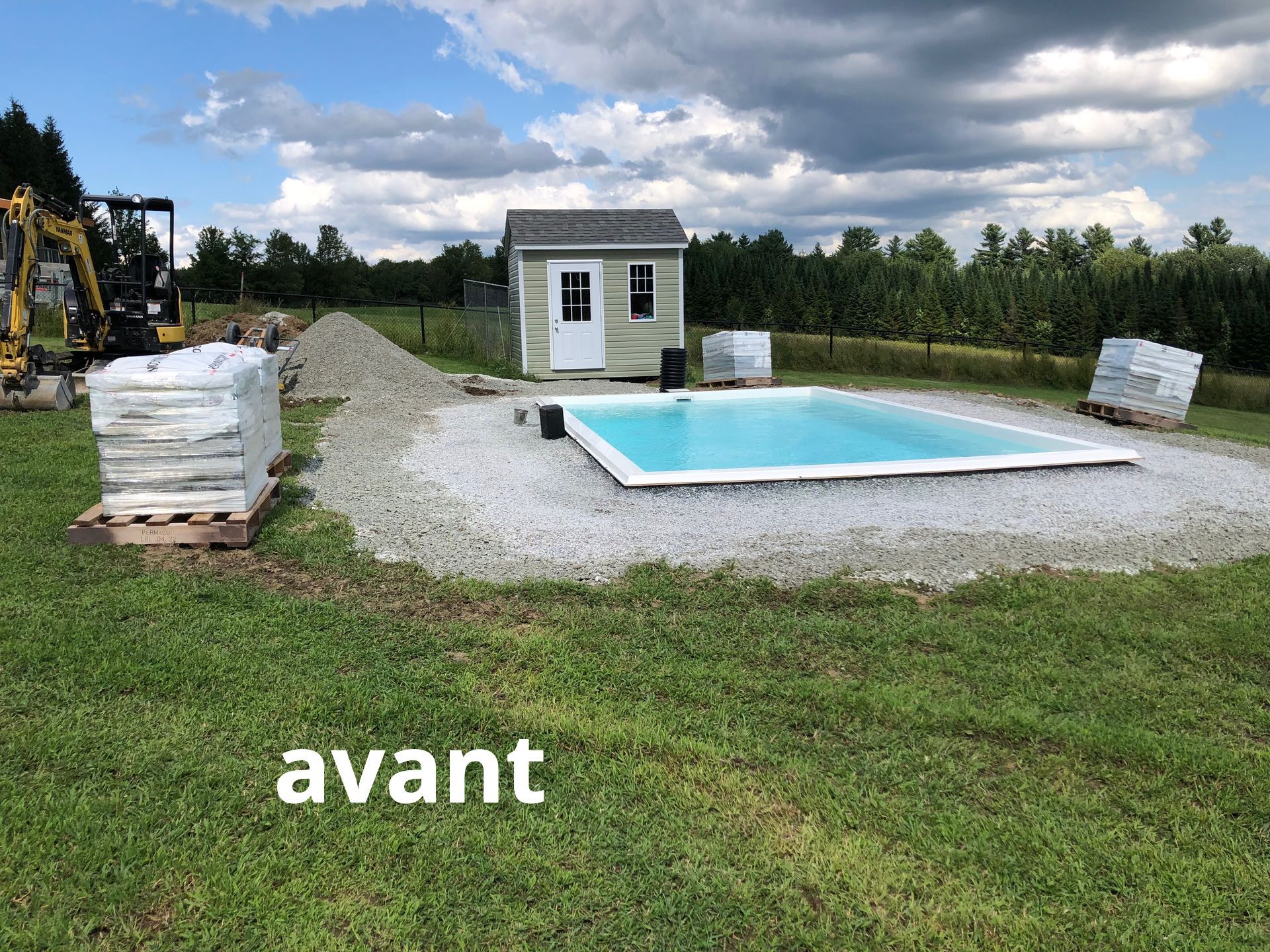 Une piscine est en cours de construction dans un champ herbeux à côté d'un hangar.