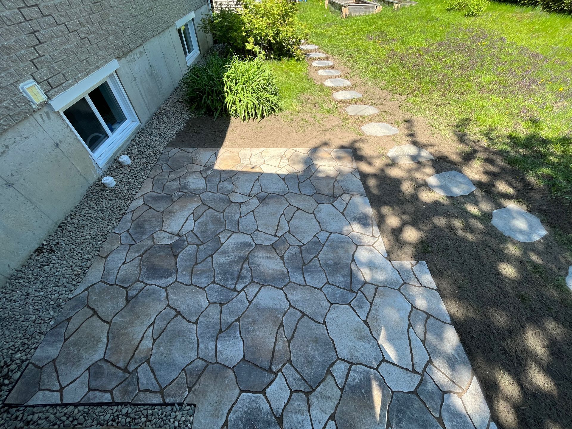 Une allée en pierre menant à une fenêtre de sous-sol à côté d'une maison.