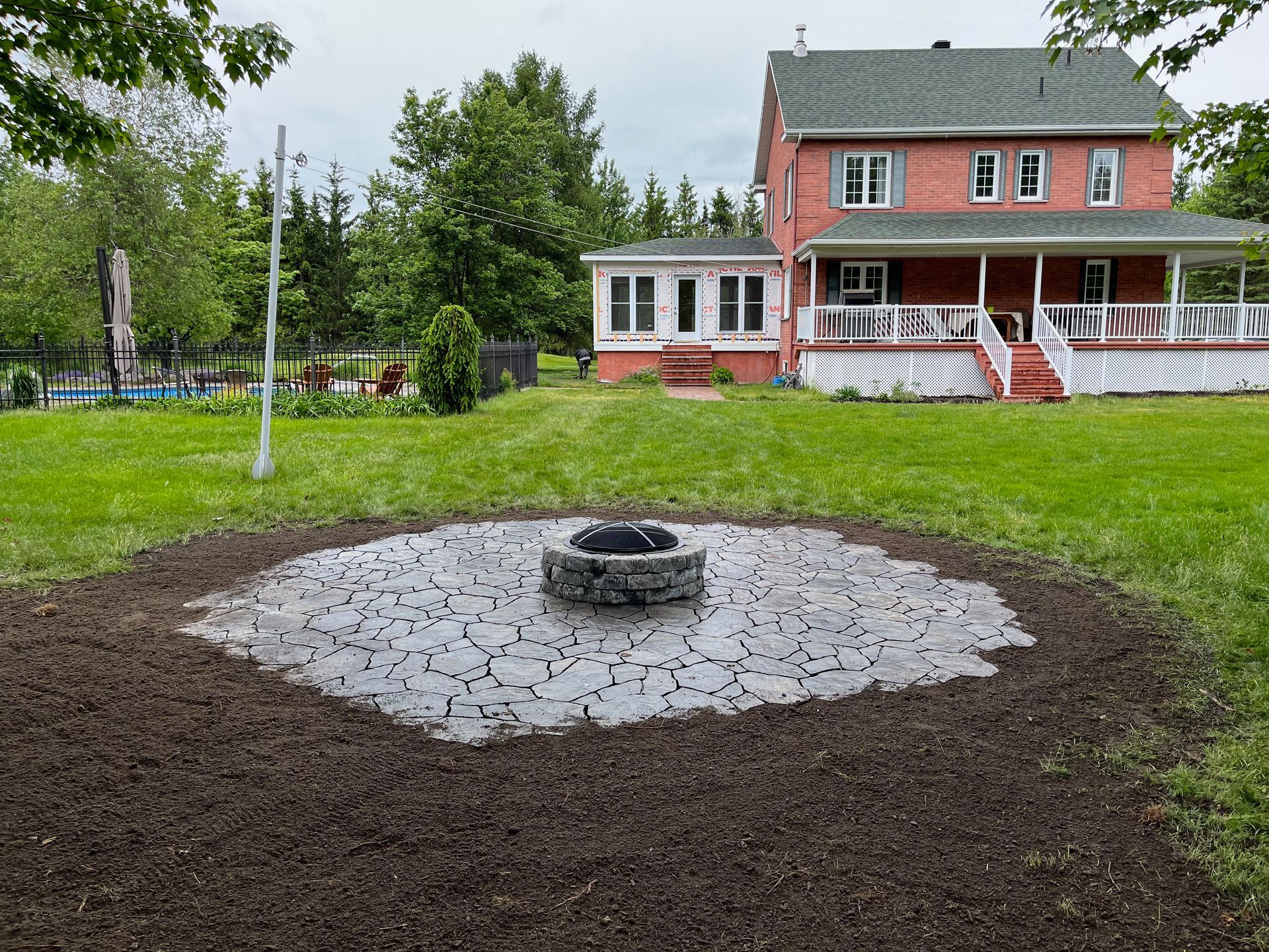 Un foyer se trouve au milieu d'un champ verdoyant devant une grande maison rouge.