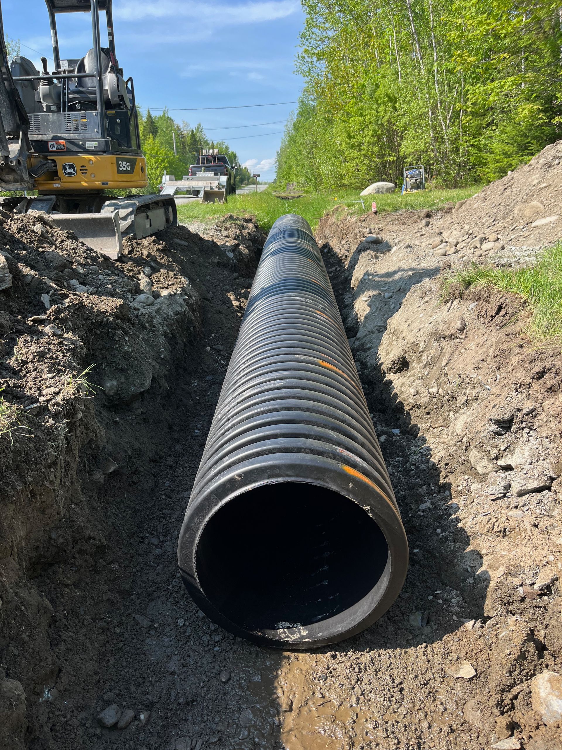 Un gros tuyau noir est posé dans la terre à côté d'un bulldozer.