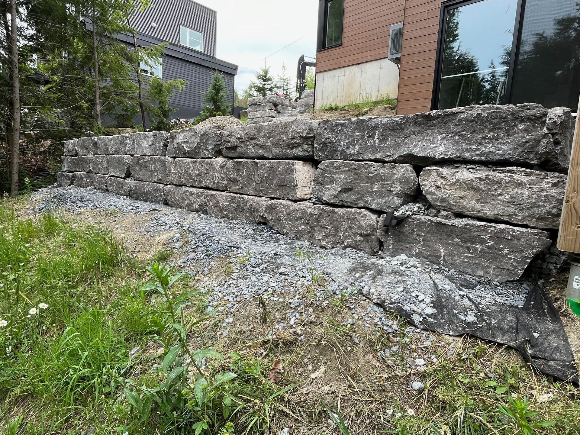 Un grand mur de pierre est assis dans l'herbe devant une maison.
