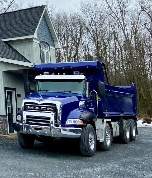 Un camion-benne bleu est garé devant une maison.