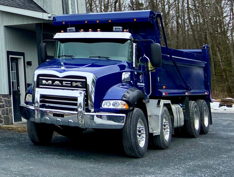 Un camion-benne bleu Mack est garé devant une maison