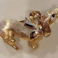 Golden Dachshund dog brooch with a bow and a pin closure.