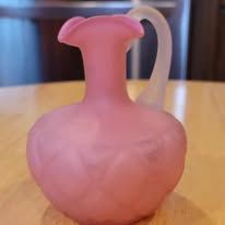 Pink frosted glass pitcher with white handle on a wooden table.