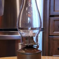 Brown antique oil lamp with glass chimney, on a wooden surface.