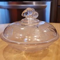 Glass butter dish with a decorative handle on a wooden surface.