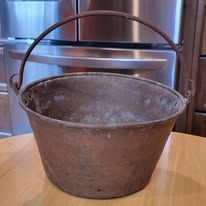 Close-up of a worn, brown, metal bucket with a handle, sitting on a wooden surface.