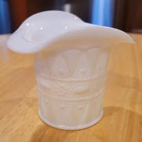 White, milk-glass top hat-shaped vase with embossed designs, sitting on a wooden surface.