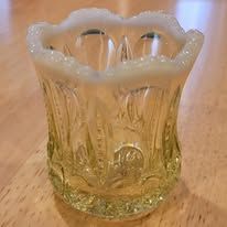 Yellow and white glass toothpick holder with scalloped rim, on a wooden surface.