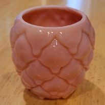 Pink, egg-shaped ceramic flower pot with a textured, overlapping pattern, sitting on a wooden surface.