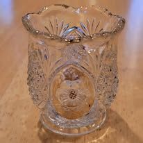 Clear, ornate glass vase with a floral design, resting on a wooden surface.
