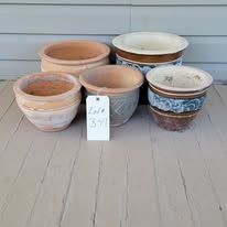 Five various terracotta and glazed ceramic flower pots on a wooden surface.