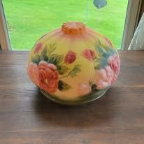 Round glass lampshade with pink flowers and yellow background, on a wooden table.