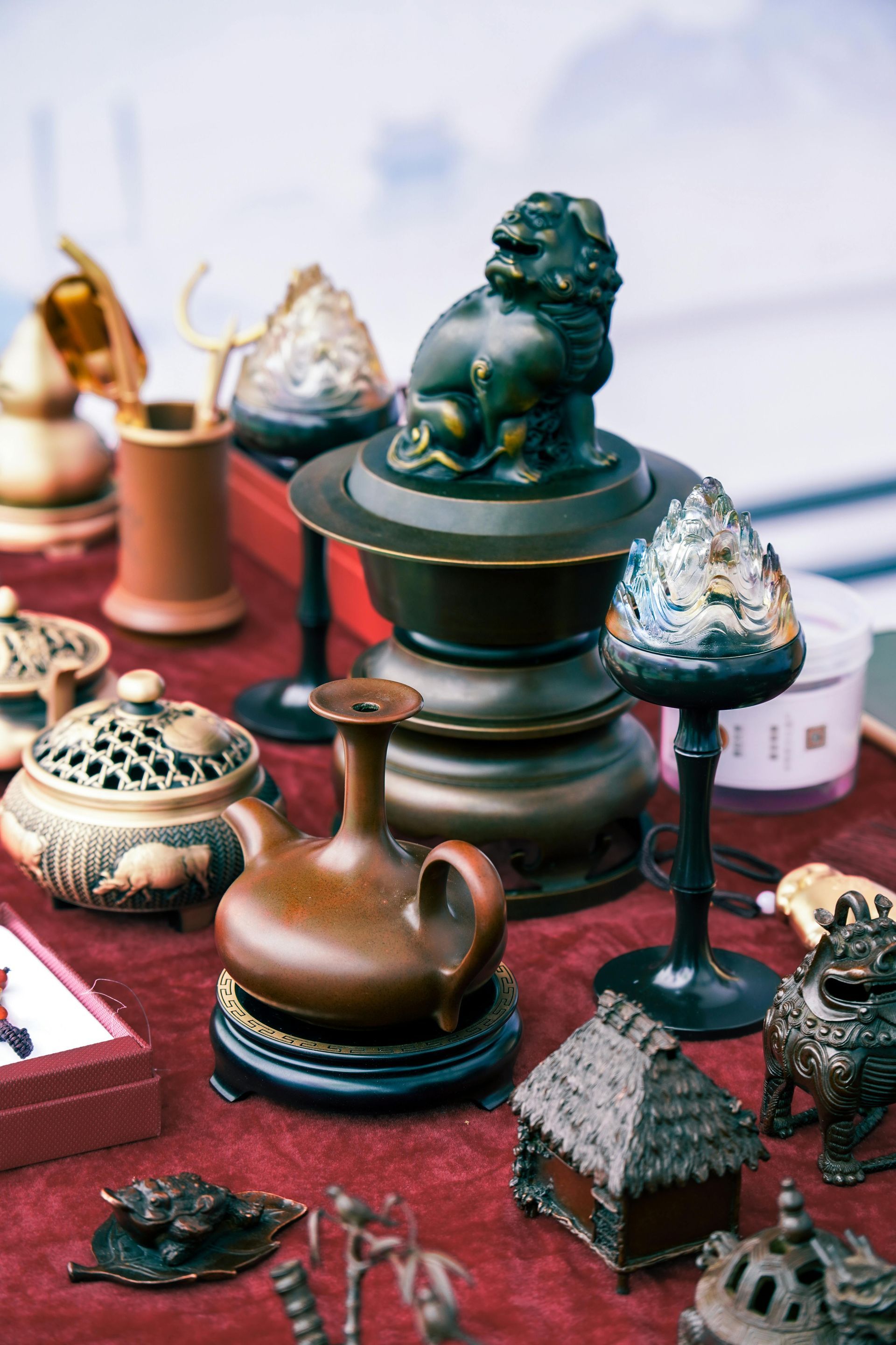 Antique display with various ornate bronze and brown objects, including vases and statues, on a red cloth.