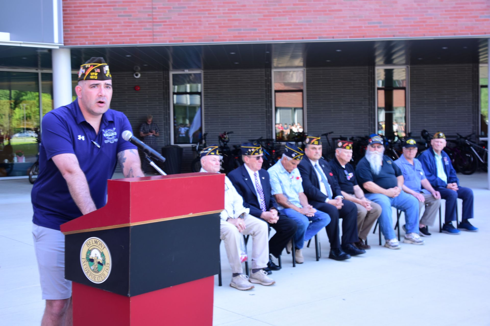 A man is standing at a podium talking to a group of men sitting in chairs.