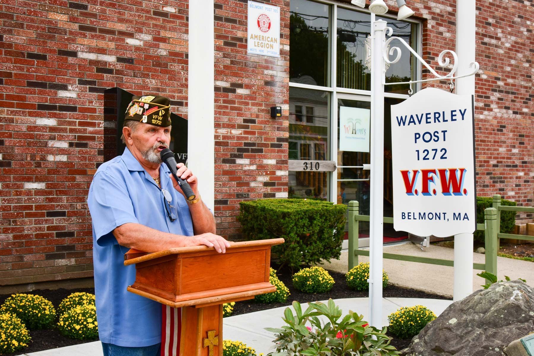 A man is giving a speech at a podium in front of a brick building.