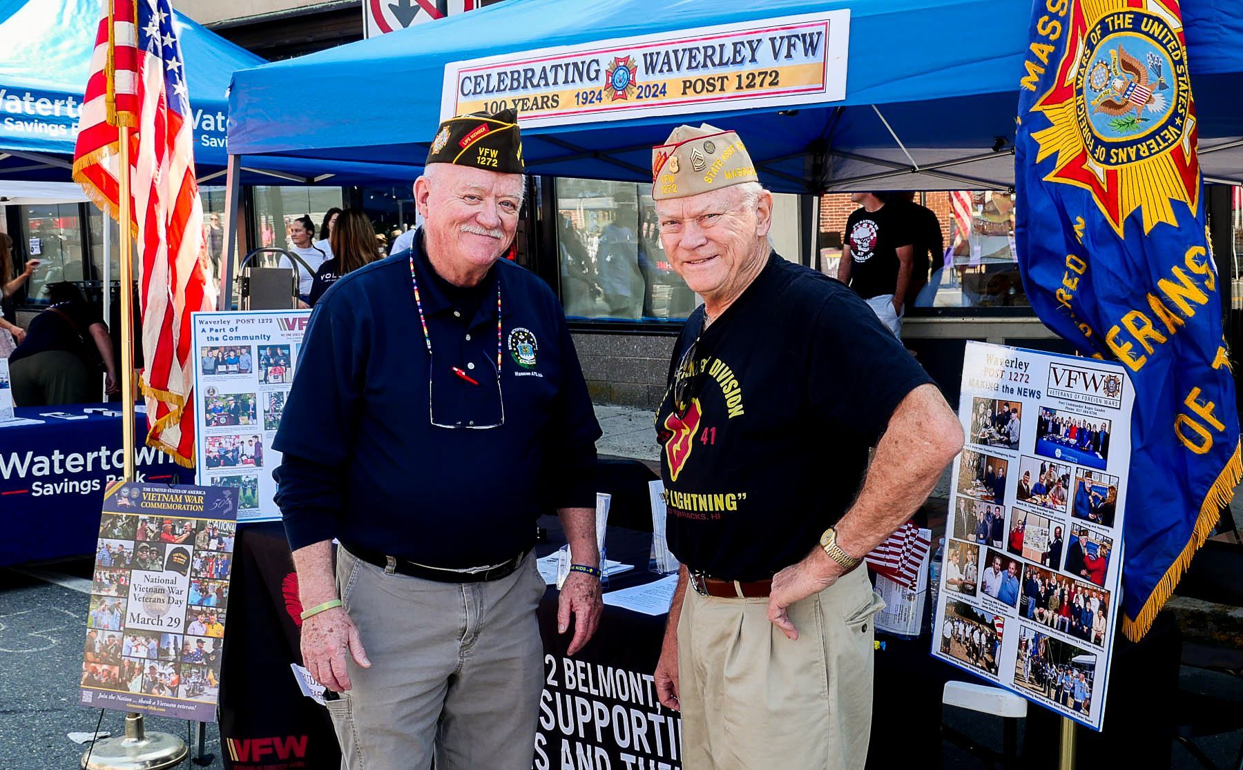 Two men are standing in front of a tent that says veterans