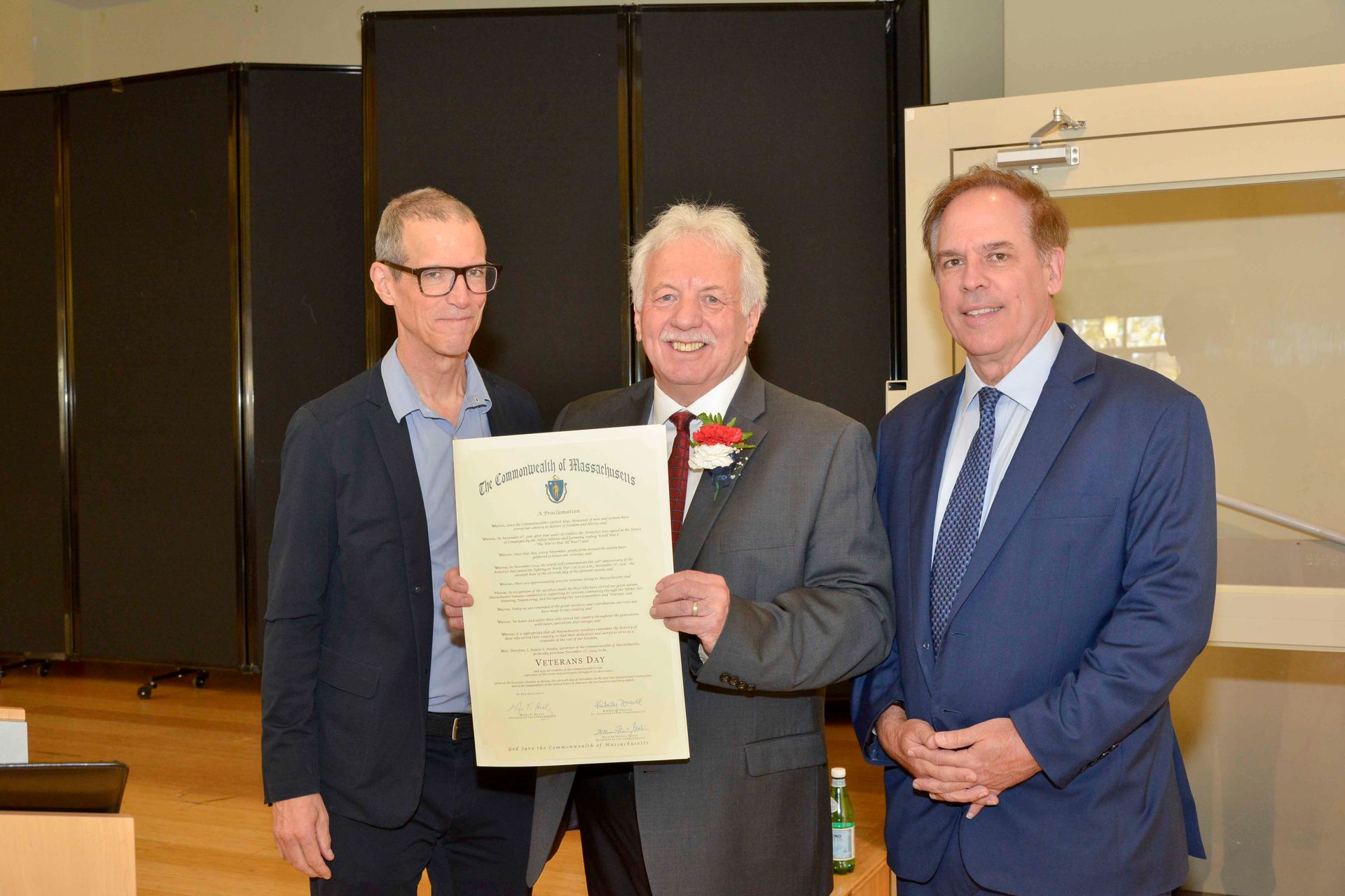 Three men in suits are standing next to each other holding a certificate.