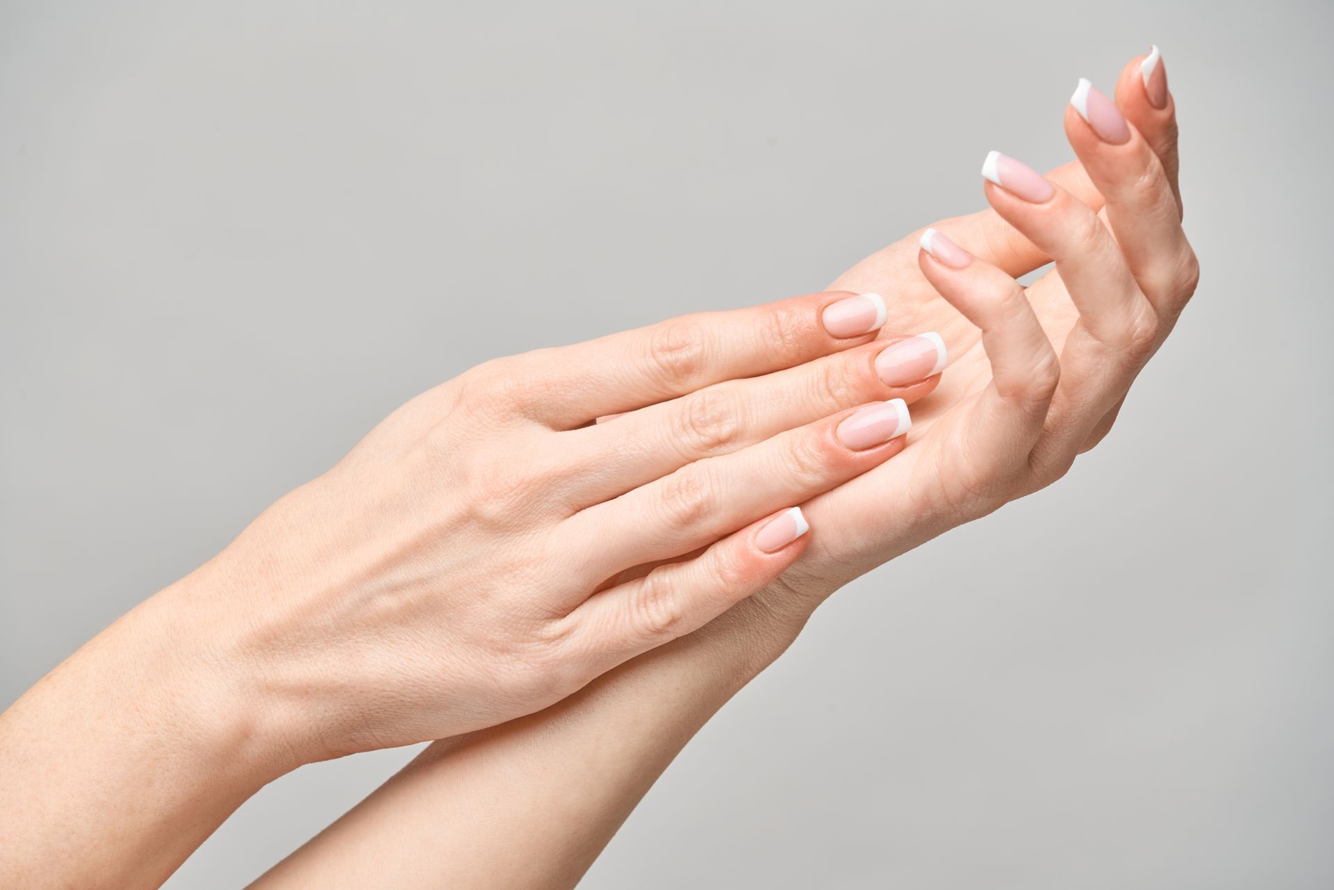 A close up of a woman 's hands with french manicure on a gray background.