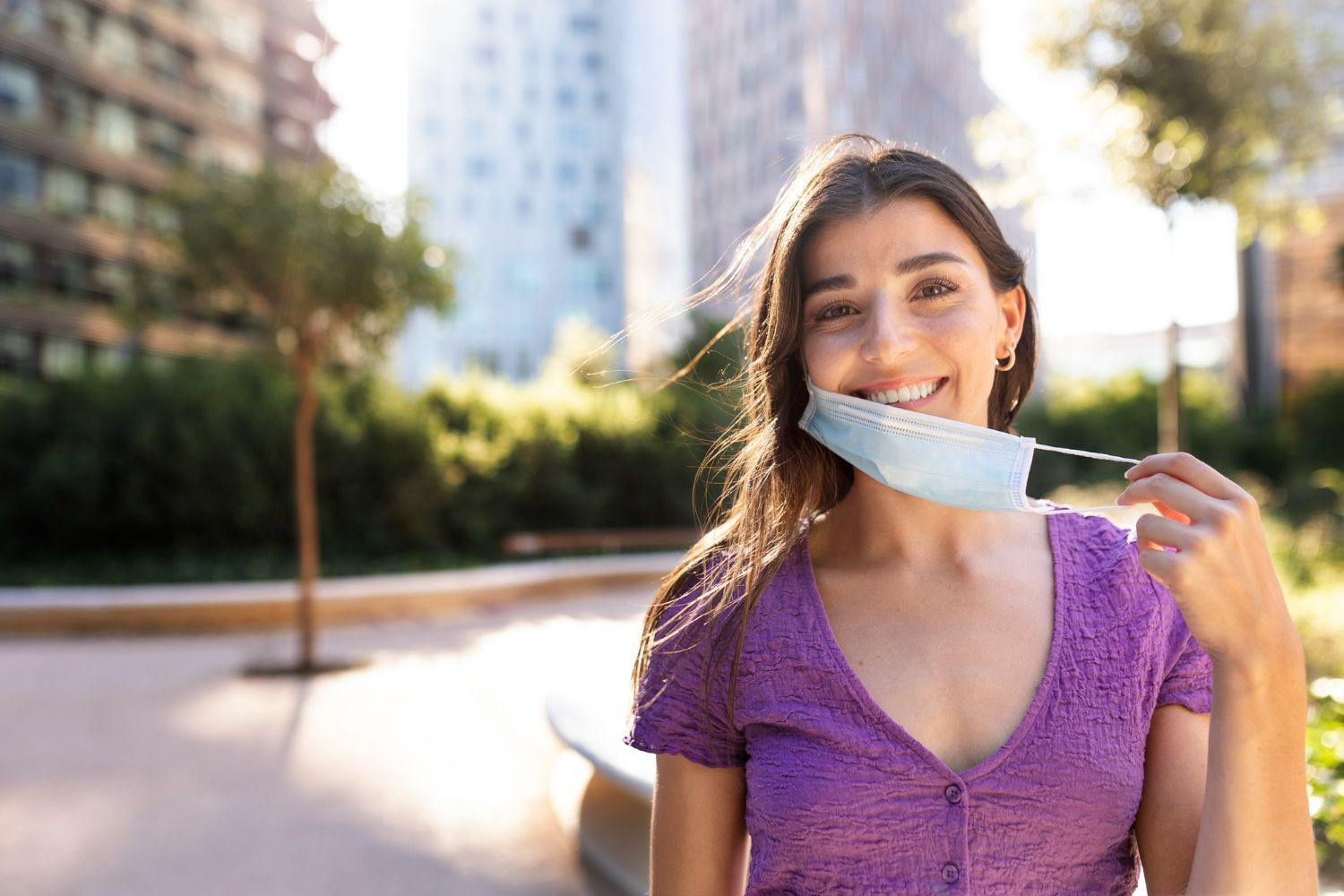 A woman is wearing a face mask and smiling in a park.