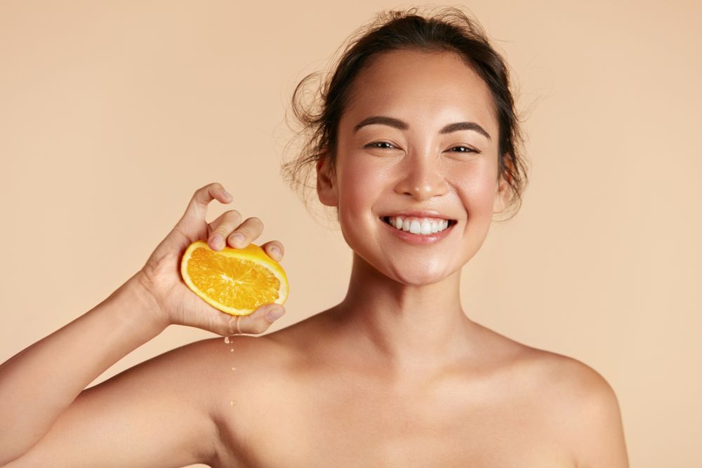 A smiling woman is holding a slice of orange in her hand.