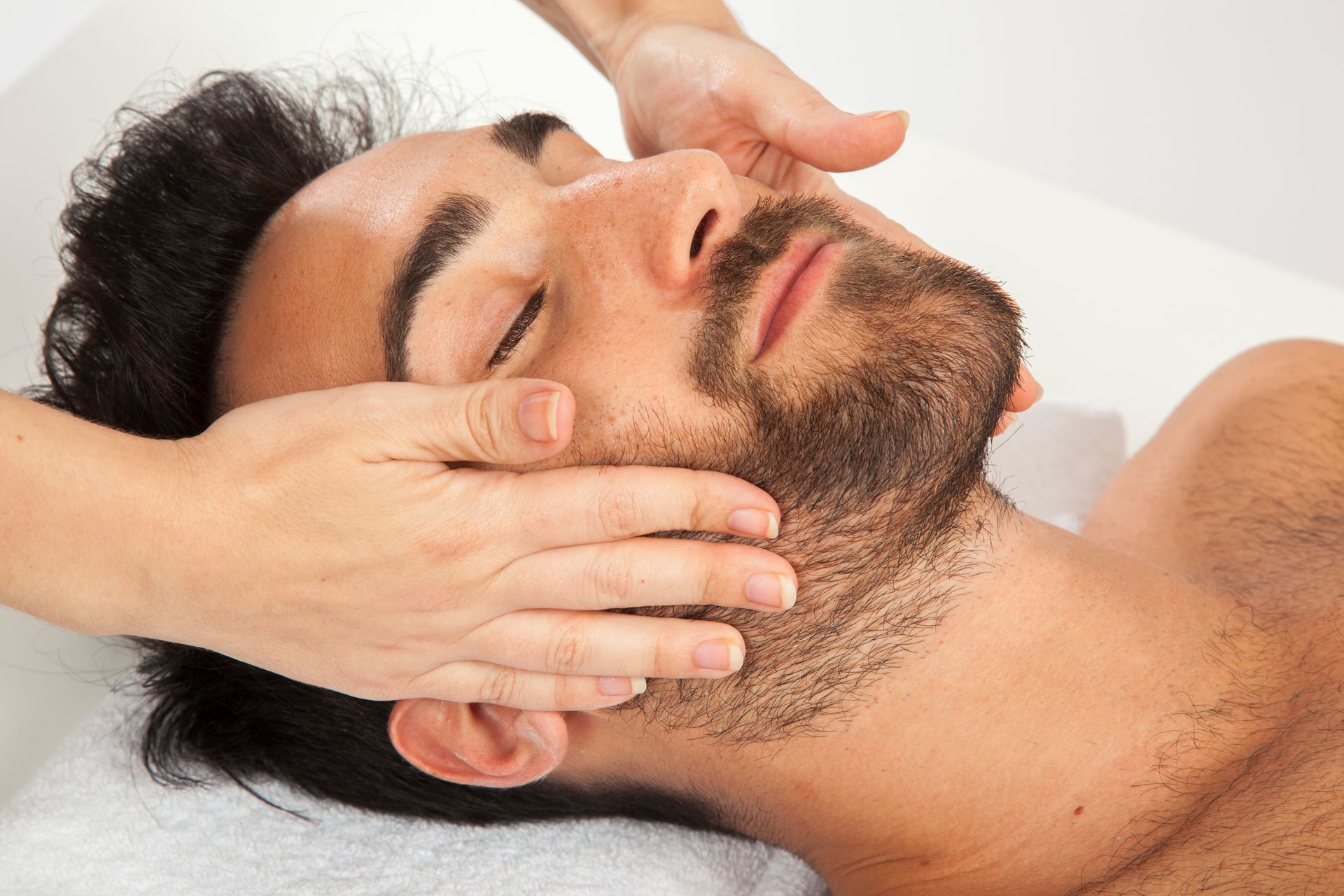 A man with a beard is getting a facial massage at a spa.